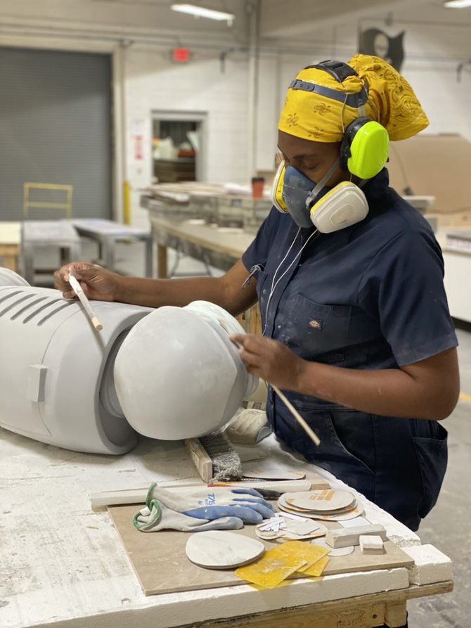 Painter wearing gasmask and Dickies coveralls applying spraypaint to unpainted statue