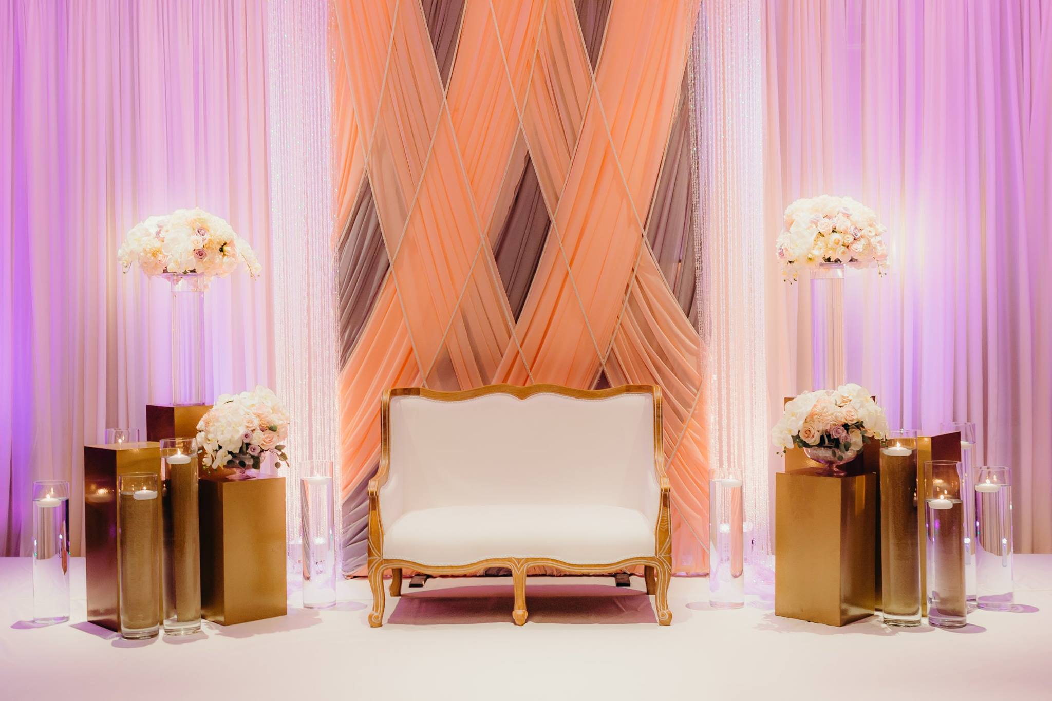 Gold wedding furniture and loveseat in front of rose, purple, and white pipe and drape setups