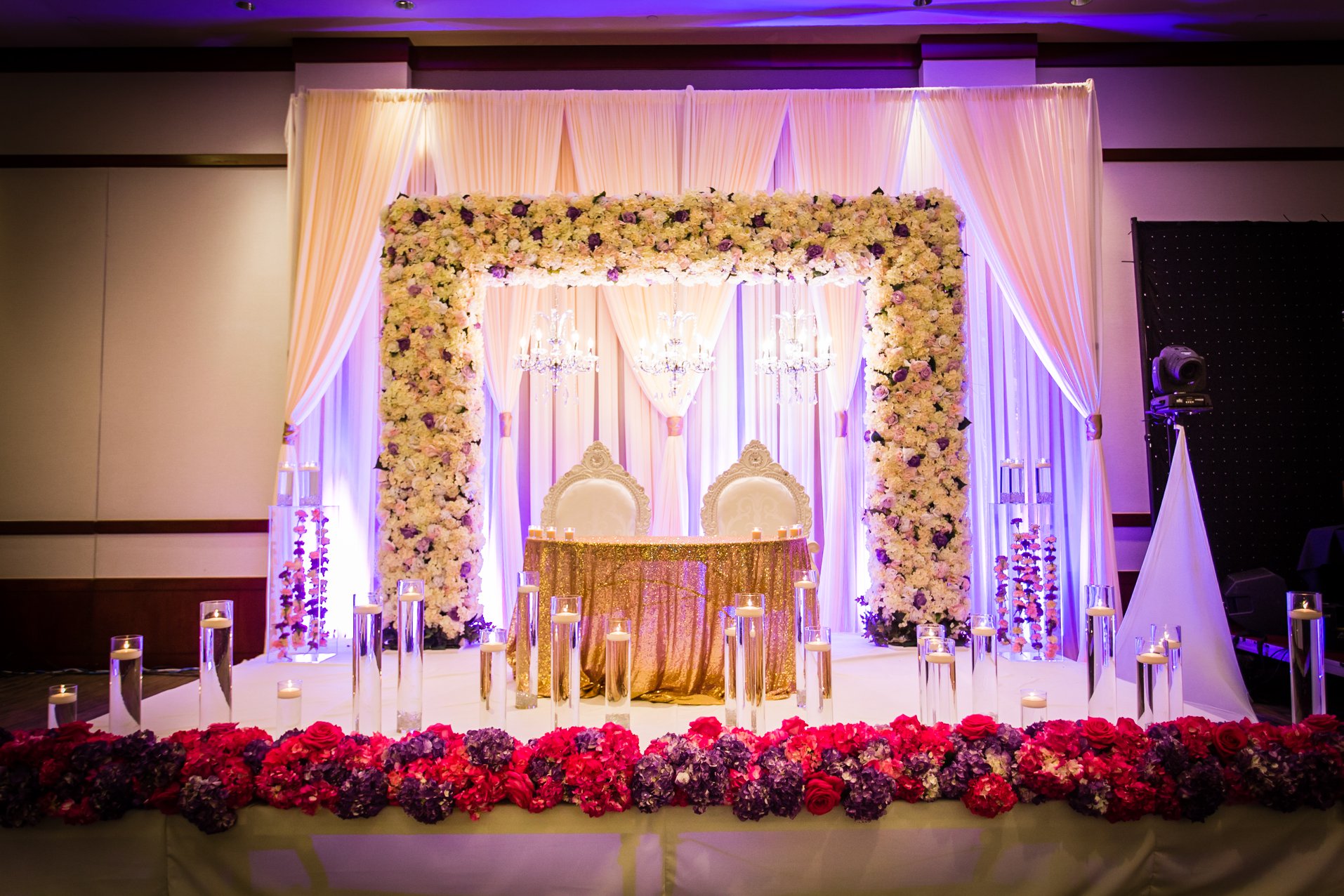 Wedding stage area with white pipe and drape, floral backdrop, and traditional decorations