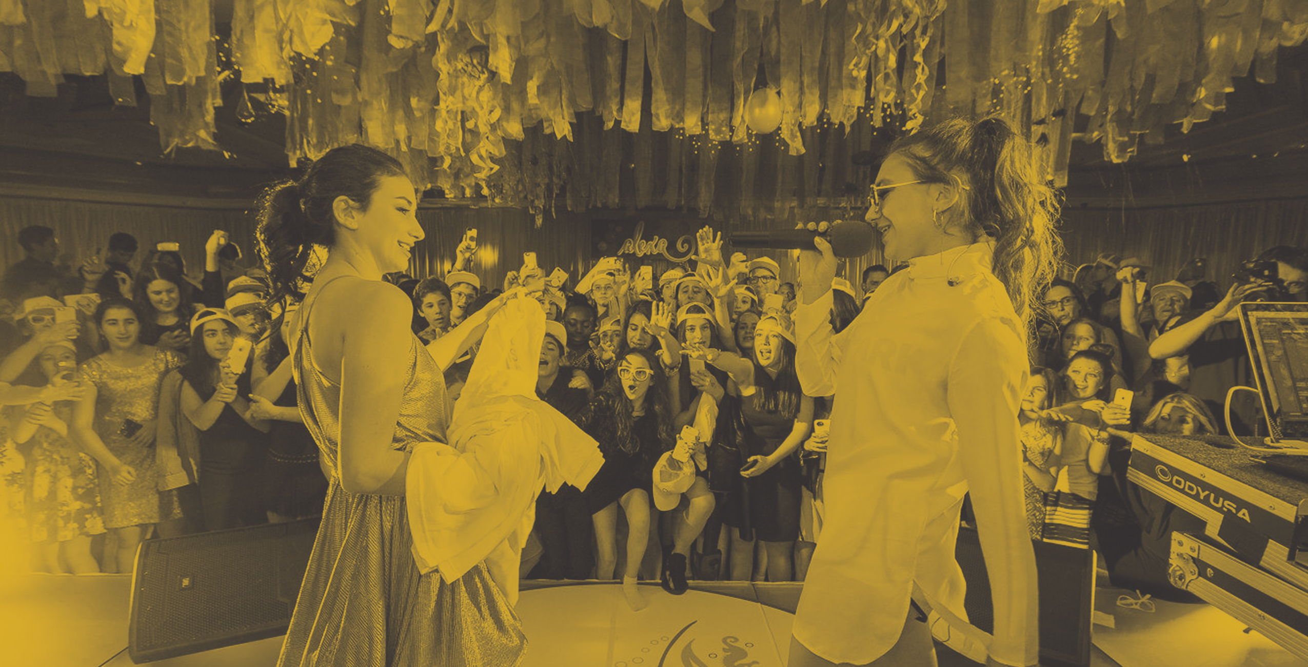 Landscape brand page header image shows a Mandell event with two event guests on stage in front of a small teen crowd behind a duotone yellow overlay treatment.