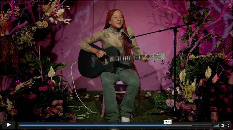 Musician performing with acoustic guitar on chair inside virtual livestreaming studio