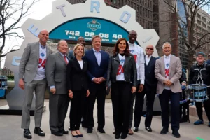 Group of officials posing in front of the NFL Draft countdown clock at 742 days in downtown Detroit